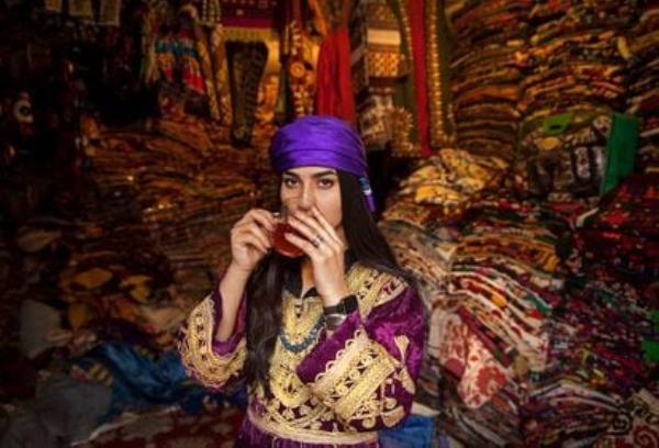 An Afghan woman in traditional garb poses while sipping tea. A photo from Hossaini’s collection, 'Pearl in the Oyster.'