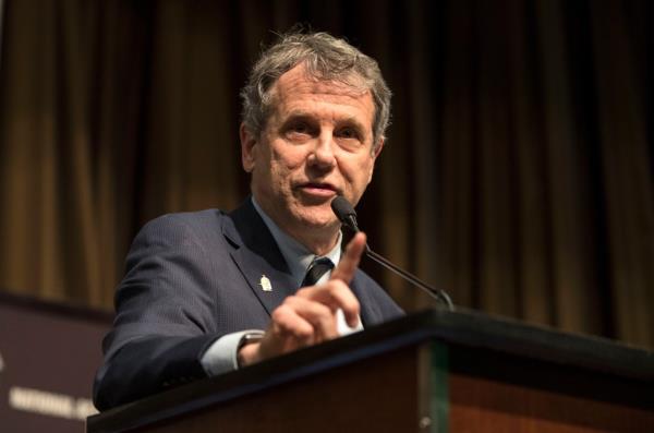 Sherrod brown in a suit standing at a podium with a microphone talking